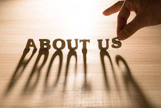 Hand arranging wooden letters spelling 'ABOUT US' on a wooden surface.